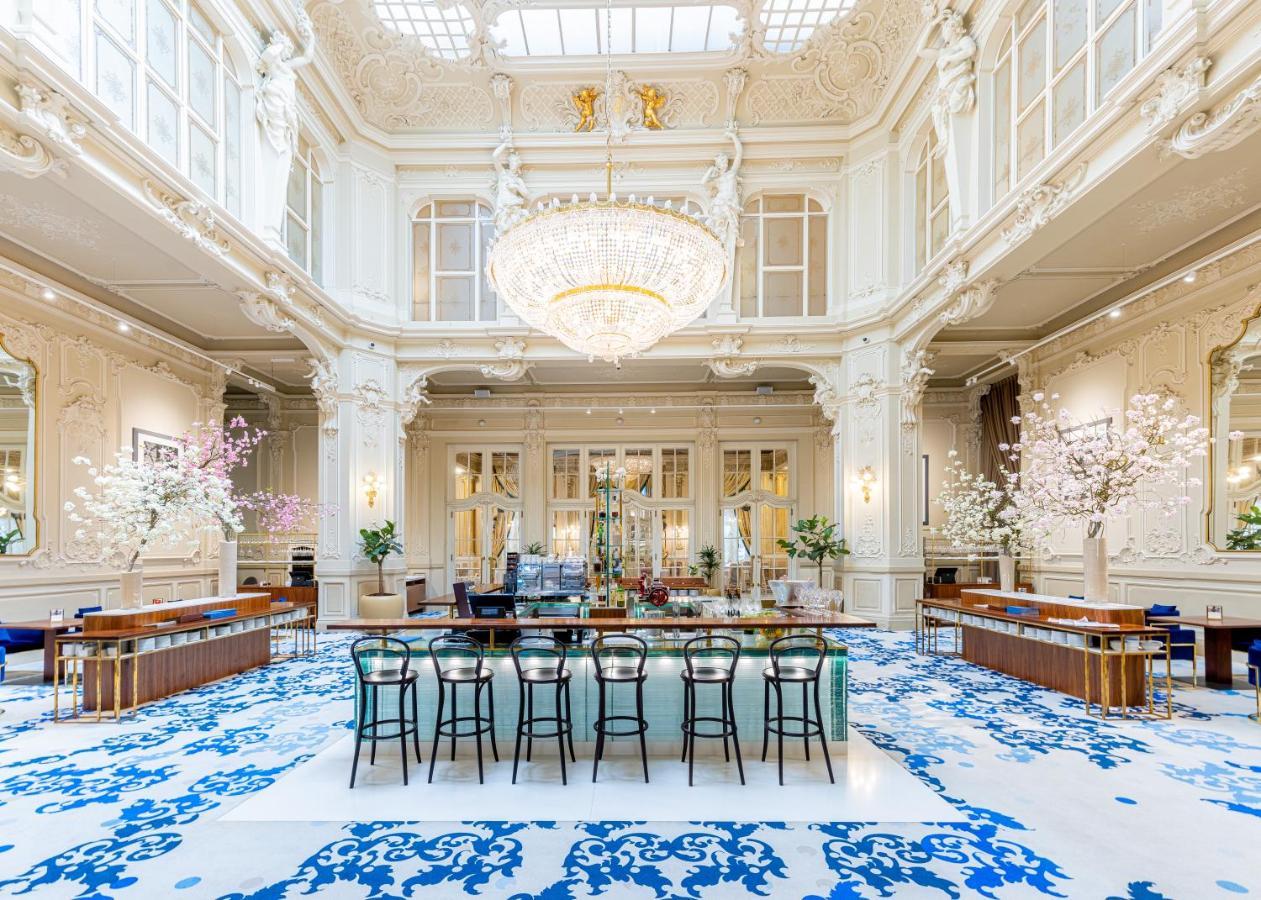 Grandhotel Pupp Karlovy Vary Esterno foto The photo shows an elegant interior space, likely a hotel lobby or a high-end establishment. The room features high ceilings adorned with ornate moldings and a large chandelier that hangs prominently from the ceiling. The space is filled with natural