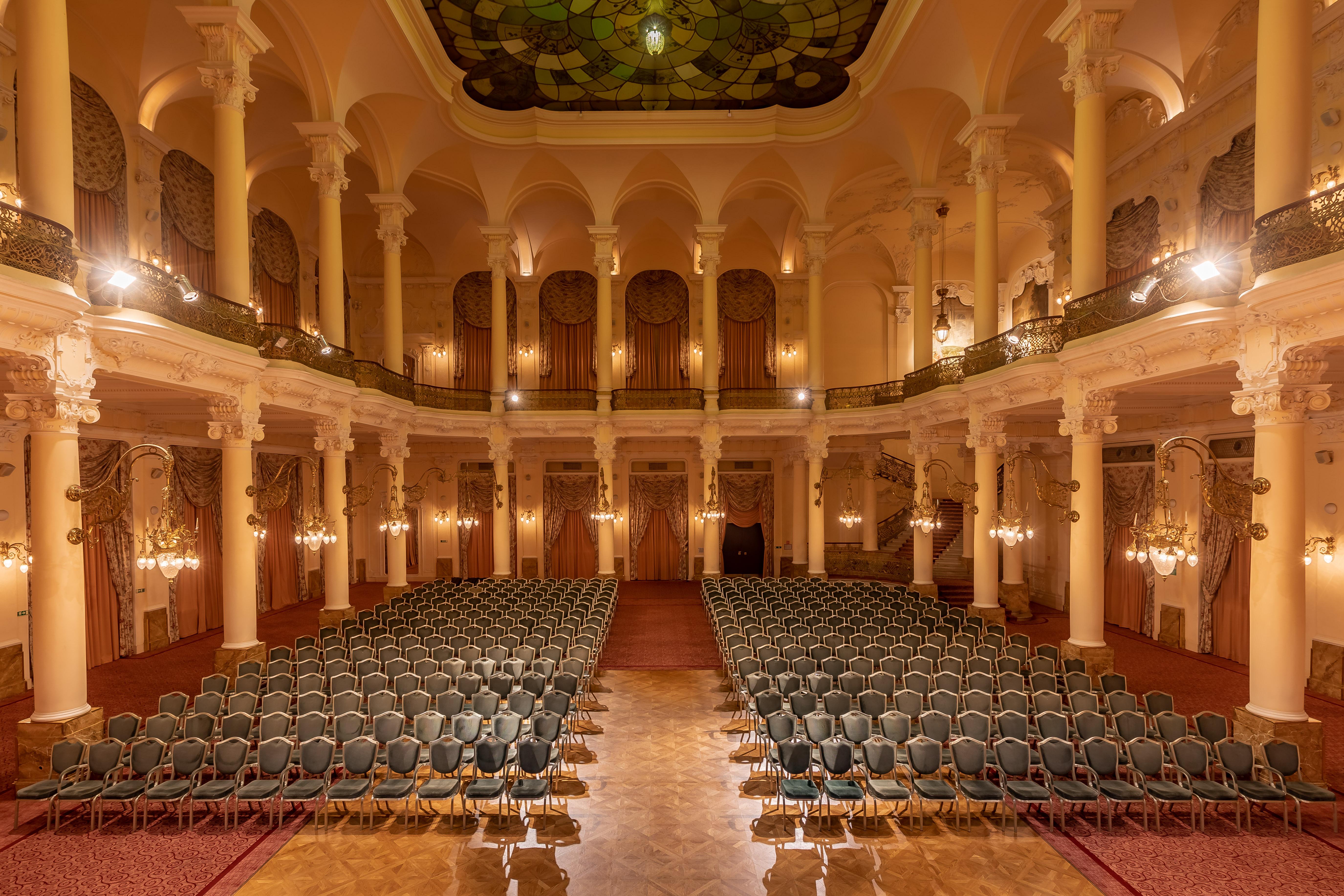 Grandhotel Pupp Karlovy Vary Esterno foto The photo shows an elegant, spacious auditorium or hall, designed for events or performances. The interior features high ceilings supported by tall, decorative columns. Rows of green upholstered chairs are neatly arranged, suggesting the space is set
