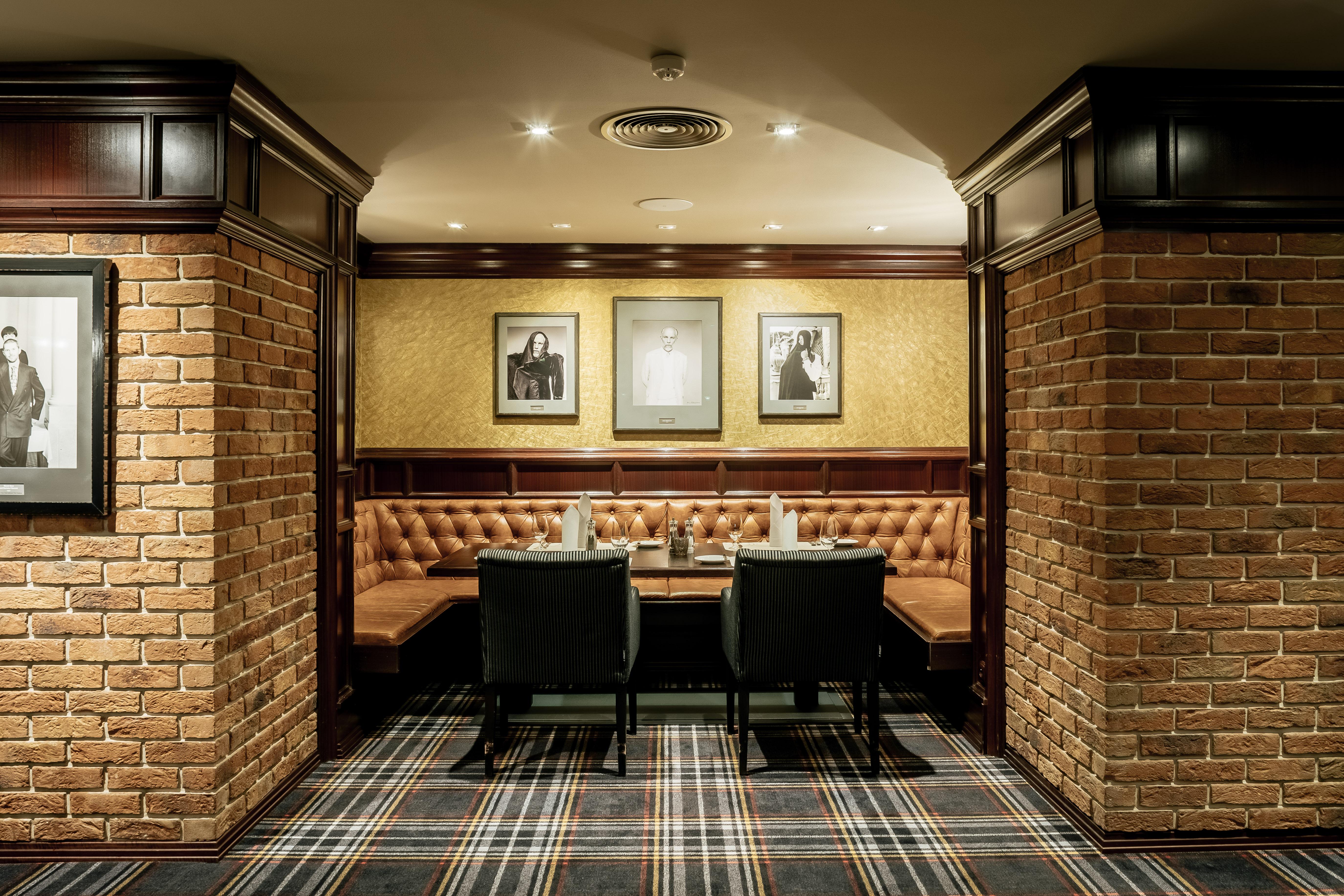 Grandhotel Pupp Karlovy Vary Esterno foto The photo depicts a cozy interior of a room, likely a restaurant or lounge. It features brick walls, giving it a rustic feel, and wooden paneling adds a touch of elegance. There are two black chairs positioned at a wooden table. The seating area is c