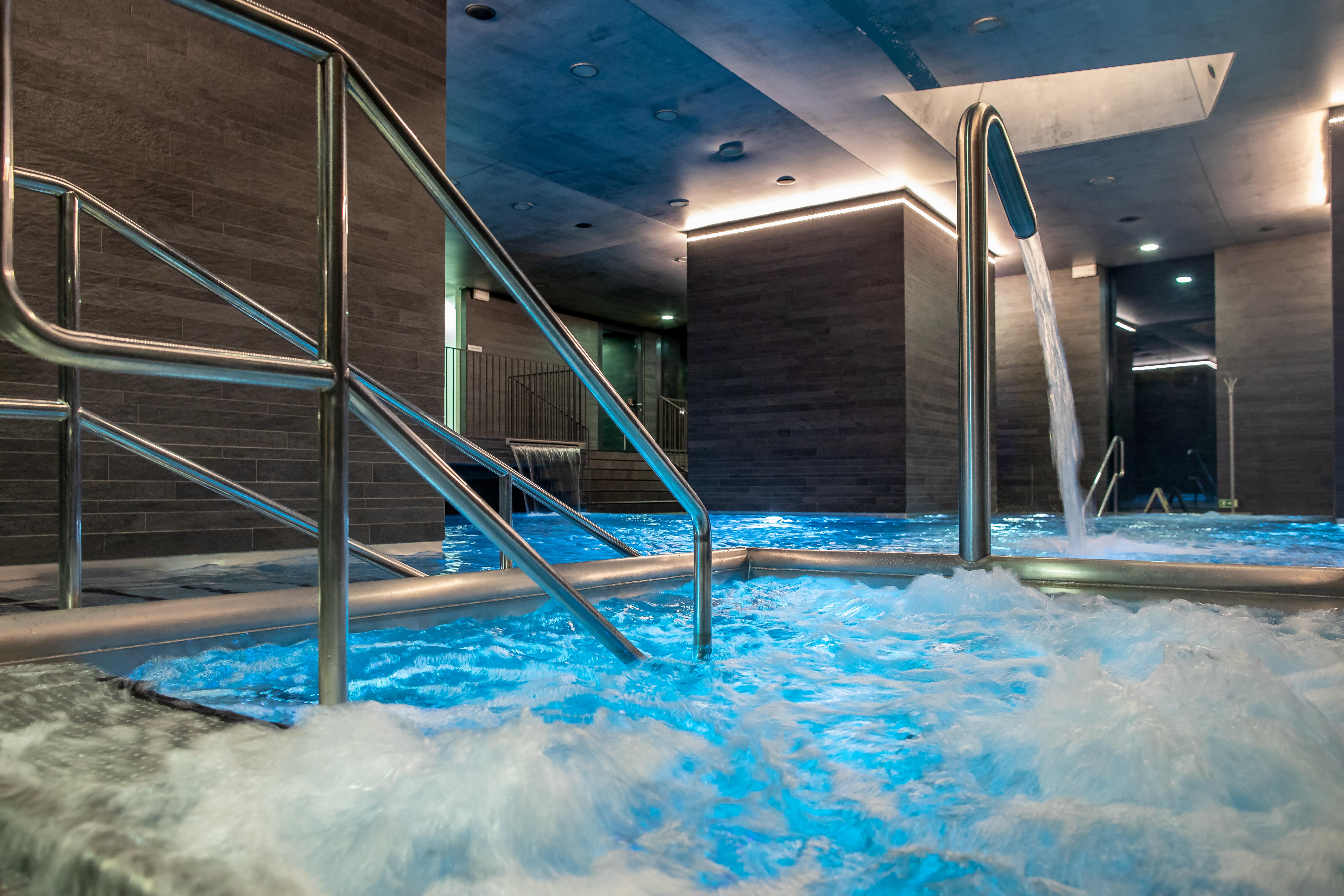 Grandhotel Pupp Karlovy Vary Esterno foto The photo shows a sleek, modern spa area featuring a hot tub or pool with bubbling, illuminated blue water. There are stainless steel handrails leading into the water. The walls have a contemporary design with a gray finish, and there are soft lights