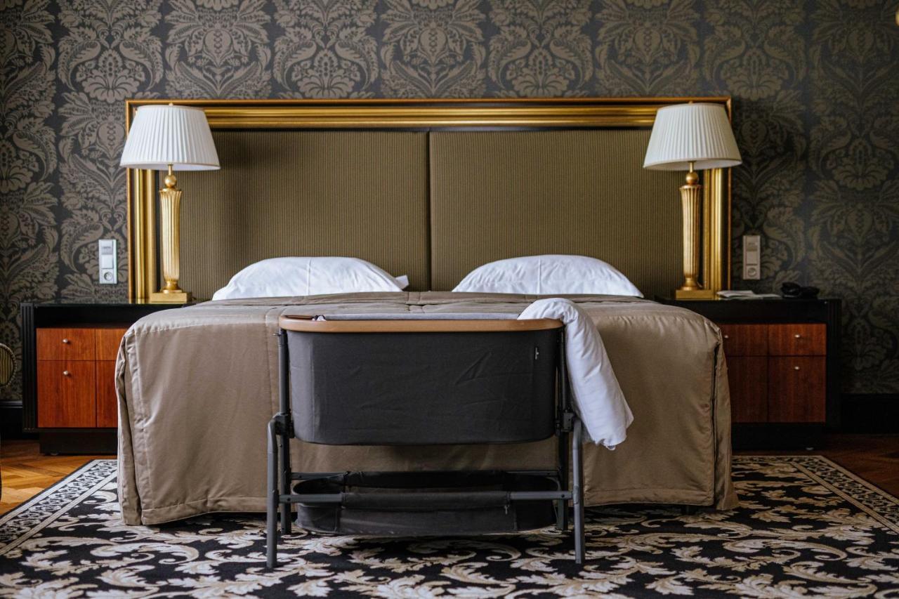 Grandhotel Pupp Karlovy Vary Esterno foto The photo shows a cozy hotel room with a stylish design. In the center, there are two beds with white pillows and a beige bedspread. Flanking the beds are two elegant lamps on side tables, and behind the beds is a large gold-framed headboard. At the 