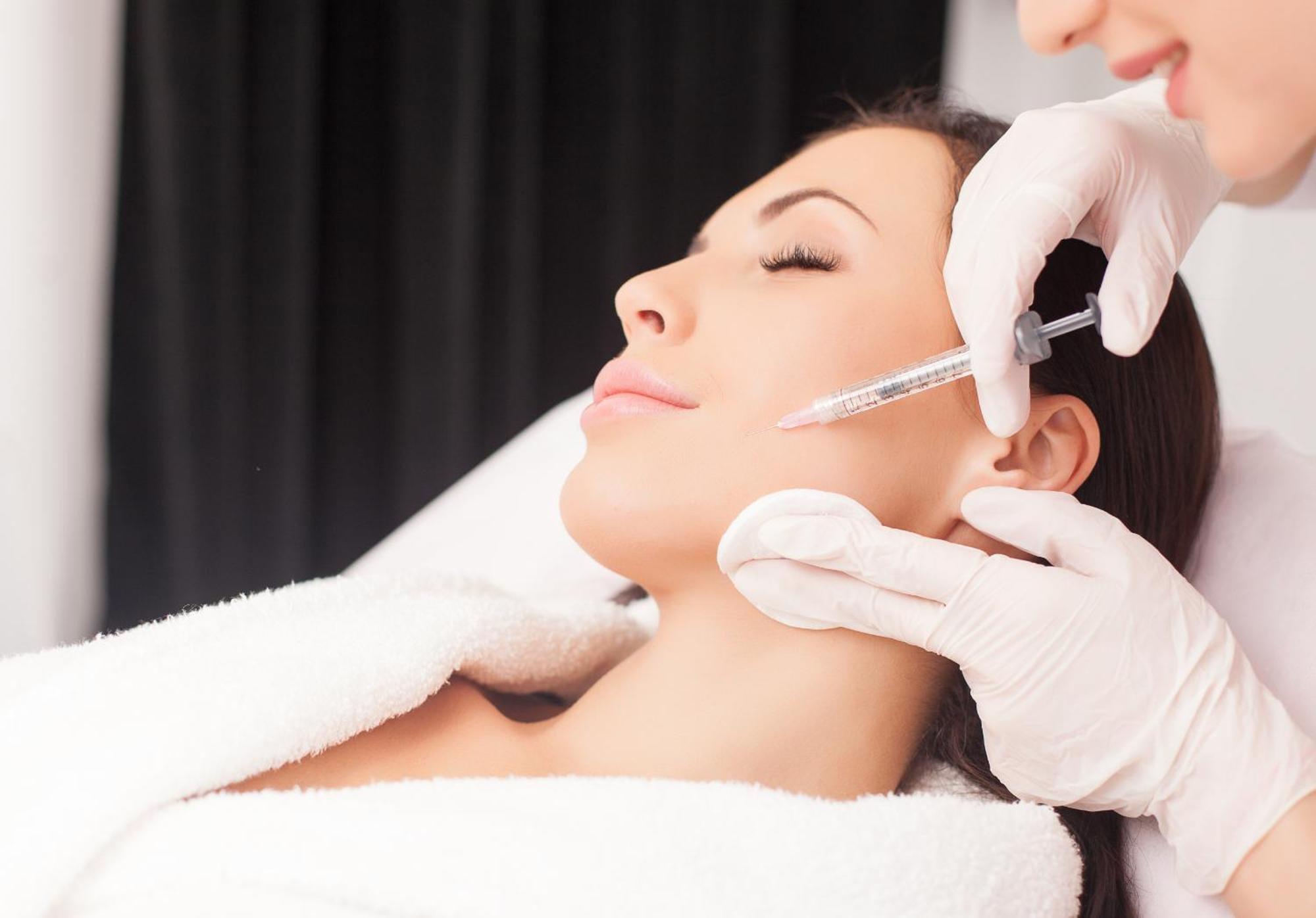 Grandhotel Pupp Karlovy Vary Esterno foto The photo depicts a woman receiving a cosmetic treatment in a spa or clinical setting. She is reclining with her eyes closed, appearing relaxed. A professional, wearing gloves, is administering an injection to her face, likely as part of a procedure 