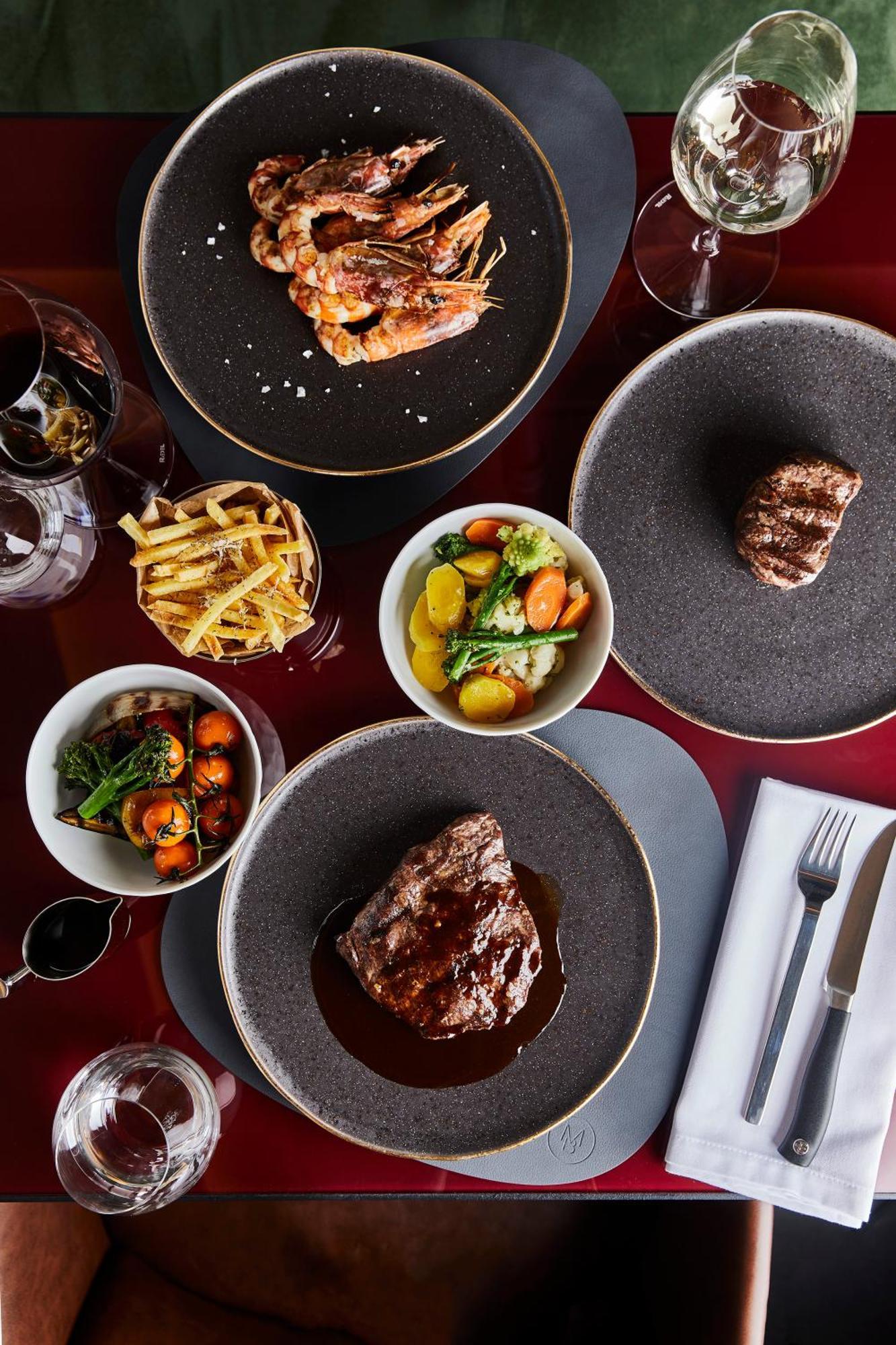 Grandhotel Pupp Karlovy Vary Esterno foto The photo features a gourmet meal spread across a dining table. Key elements include:

1. **Main Dishes**: There are two pieces of grilled steak, one prominently displayed at the bottom and another slightly obscured at the top right, both garnished w