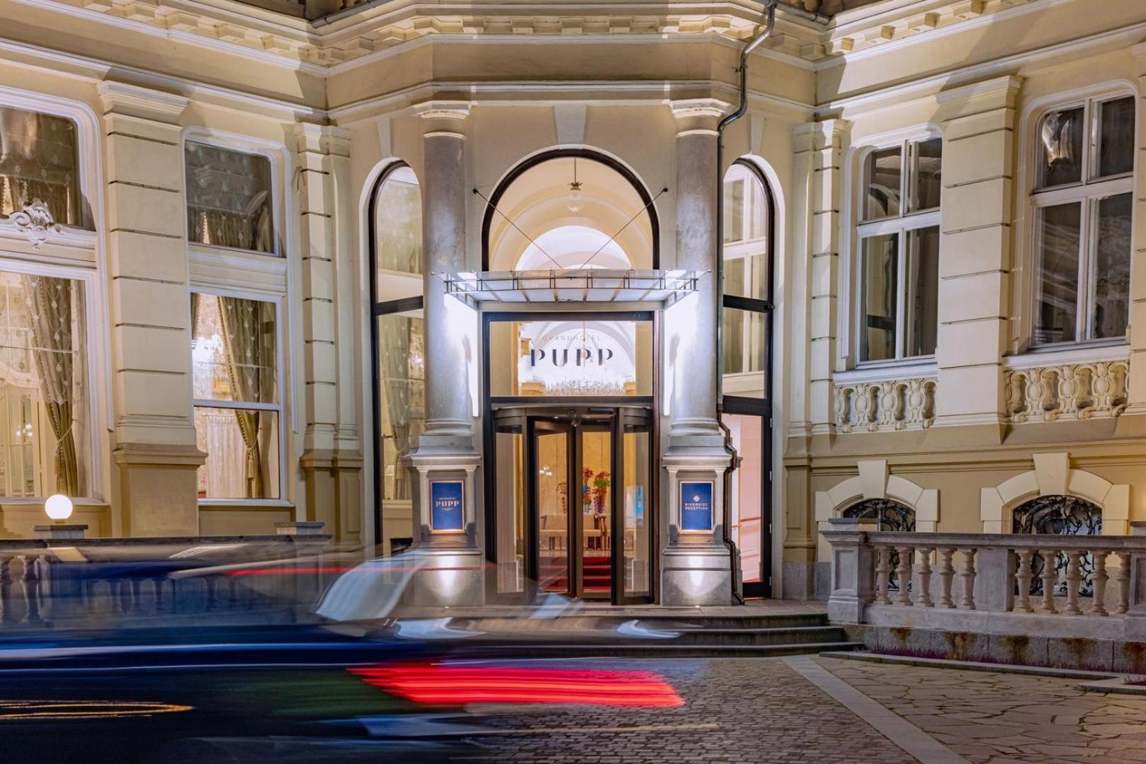 Grandhotel Pupp Karlovy Vary Esterno foto The photo depicts the entrance of a building, likely a theater or cultural venue, at night. The facade features a classic architectural style with decorative elements. The entrance has a pair of double doors framed by large windows, and there is a pr