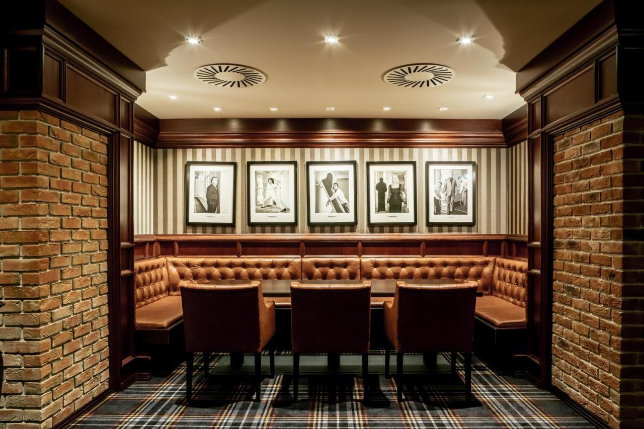 Grandhotel Pupp Karlovy Vary Esterno foto The photo shows an elegantly designed room, likely a private dining or meeting area. It features a circular seating arrangement with a table surrounded by plush, brown leather chairs. The walls are adorned with a combination of exposed brick and stri